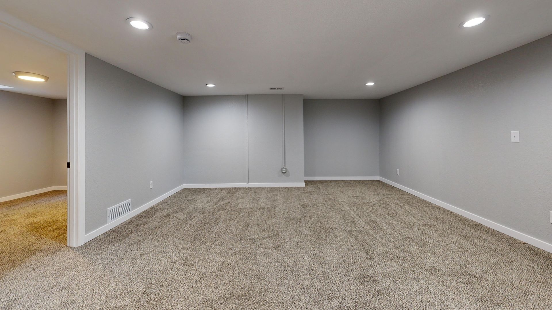 Open basement room with neutral gray walls and plush carpeting, ideal for remodeling.